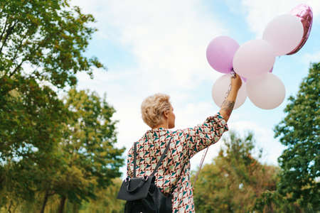 Lovely woman with backpack walking happy with pink balloons in the park. Freedom and healthy women...