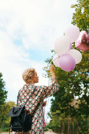 Lovely woman with backpack walking happy with pink balloons in the park. Freedom and healthy women...