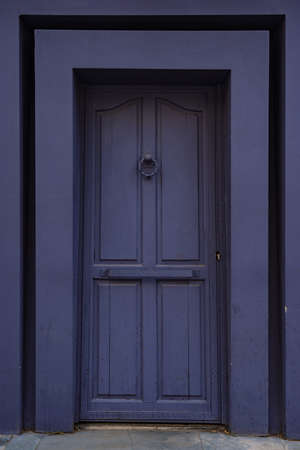 An antique knocker on a purple wooden door.