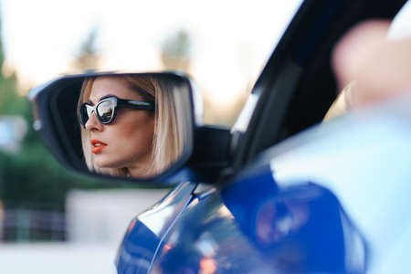 Young woman driver looking in car side view mirror, making sure line is free before making a turn.