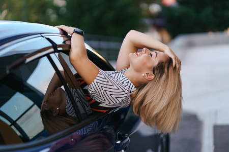 Cheerful Caucasian woman drives through the picturesque sunny city and waves her arms while...