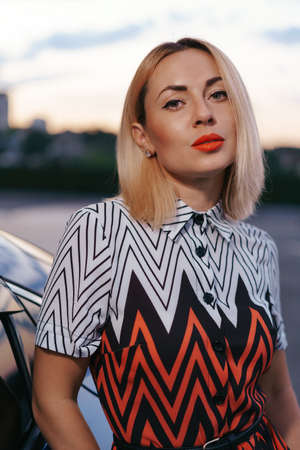 Stunning young woman close up portrait posing in front of her car outdoors, ownership driver