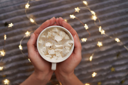 Female hands hold a cup of coffee with marshmallow on gray background with glowing lights. Flat lay, top viewの写真素材