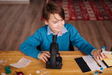 Distance online education, internet learning. First grade boy studying at home using microscope,...