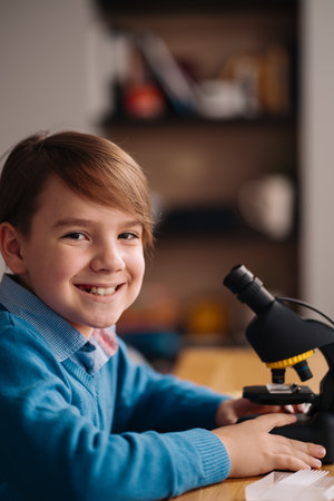 Distance online education, internet learning. First grade boy studying at home using microscope, making notes, biology online lessonの写真素材