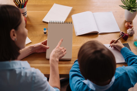 Aunt and nephew do homework together. Women explain kid writes in notebook. Schoolboy studying at home. Primary education, childhood. Copy space on notebookの写真素材
