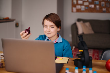 A Preteen boy uses a laptop to make a video call with his teacher. The Screen shows an online...