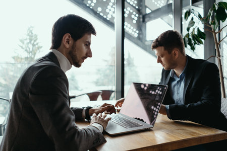 Two young businessman having a successful meeting at restaurant with a modern interior while using laptopの写真素材