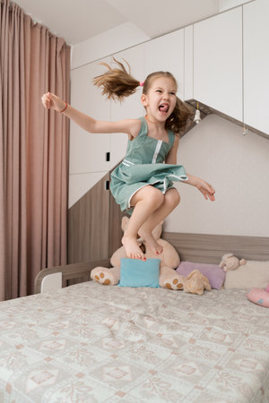 Happy funny little child girl in motion jumping on bed alone flying in air feeling joy, cheerful cute active kid having fun playing in bedroomの写真素材