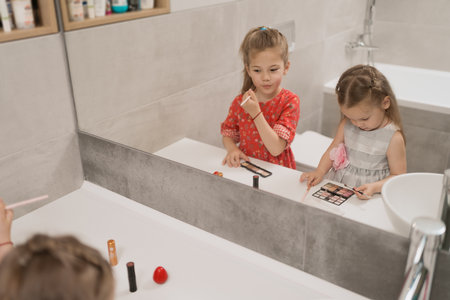 Lovely little girls applying makeup using the bath mirror, they want to be beautiful like mama.の写真素材