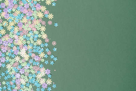 Festive green background with colorful flowers with copy space. Multi-colored small artificial flowers. Flat lay, top view.の写真素材