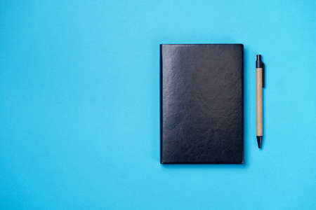 Black leather notebook on a paper blue background, notepad mock up, top view shotの写真素材