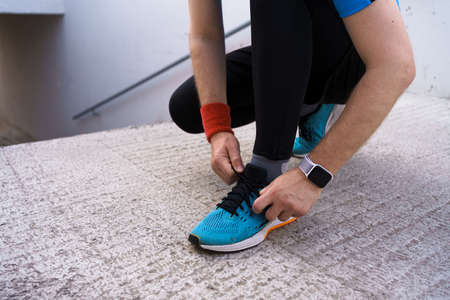 Runner is tying his running shoes. Man shoelace, his blue sneakers with smartwatch on his wristの写真素材