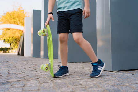 Close up legs in blue sneakers with green skateboard. Active urban lifestyle of youth, training, hobby, activity. Active outdoor sport for kidsの写真素材