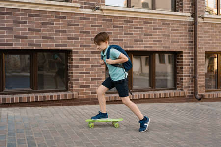 Happy young boy playing on skateboard in the city, Caucasian kid riding penny board on buildings...