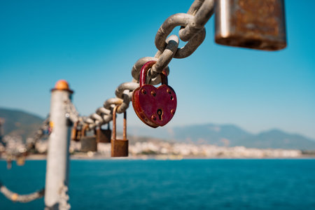 Red heart padlock on chain in front of blue sea and lighthouse, symbol of eternal loveの写真素材