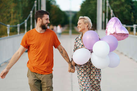 Cheerful lovely couple walking happy on bridge with their dog and pink balloons smilingの写真素材