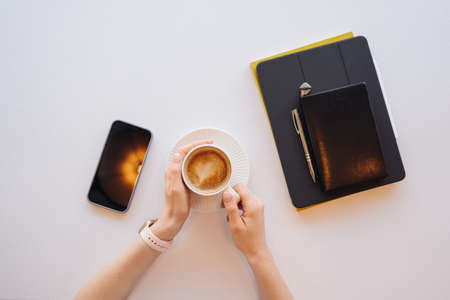 Woman hands holding cup of coffee, adigital tablet with black screen for advertisement. Top view on female palms, latte, phone, smartphone on wooden table background.の写真素材