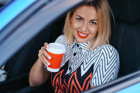 Modern blonde woman having a coffee to go while driving in the city