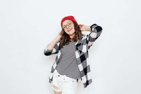 Indoor shot of good looking young Caucasian teenager girl with broad smile, being in good mood, wears round glasses, poses against white background.の写真素材