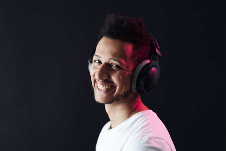 Smile Young African American man portrait wearing headphones and enjoy music over black Background with copy space. Red light reflection on face.の写真素材