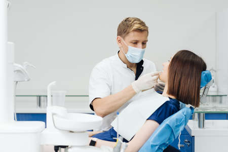 Close up portrait of beautiful young lady sitting in dental chair while stomatologist hands in sterile gloves holding tooth samples. She is smilingの写真素材