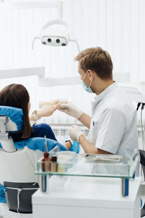 Young lady sitting in dental chair while stomatologist hands in sterile gloves holding tooth samples. She is smiling communicating and discussing with the dentistの写真素材