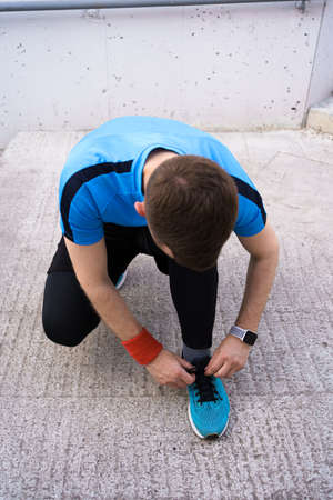 Runner is tying his running shoes. Man shoelace, his blue sneakers with smartwatch on his wristの写真素材