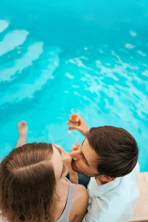 Young beautiful couple kissing while celebrating on the pool with glasses of sparkling wineの写真素材