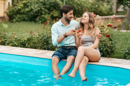 Summer holidays, people, romance, dating concept, couple drinking sparkling wine while enjoying time together sitting at the poolの写真素材