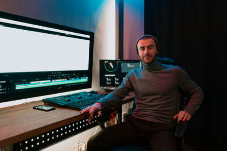 Attractive Male Video Editor Works with Footage or Video on His Personal Computer, he Works in Creative Office Studio or home. Neon lightsの写真素材