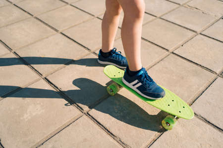 Close up legs in blue sneakers riding on green skateboard in motion. Active urban lifestyle of...