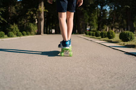 Close up legs in blue sneakers riding on green skateboard in motion. Active urban lifestyle of...