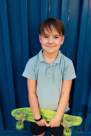 Portrait Young cool smiling BOY in blue polo posing with PENNY BOARD in the hands on a blue...