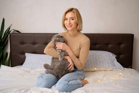 Pets, morning, comfort, rest and people concept - happy young woman with cat in bed at homeの写真素材