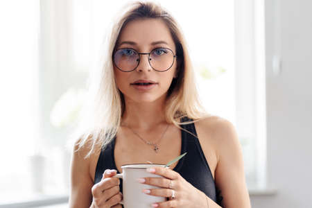 Beautiful young Caucasian woman enjoying a cup of tea at home. Female wearing glassesの写真素材