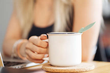 Young Caucasian woman hand holding a white cup of tea at home.の写真素材