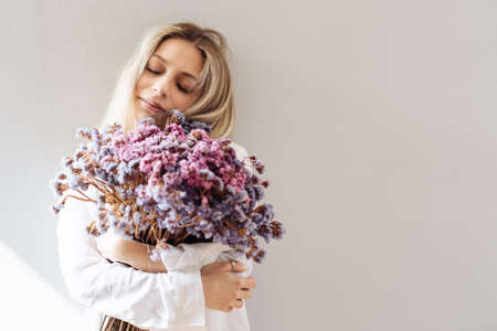 Portrait of young girl in white shirt, holding a big bouquet of dried flowers over gray background splashed by lines of lightの写真素材