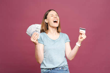 Close up portrait of a smiling woman in blue tshirt holding a credit card in one hand and cash in...
