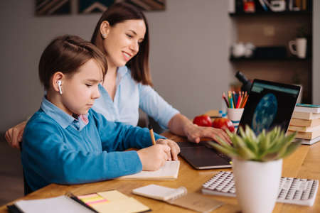 A Preteen boy uses a laptop to make a video call with his teacher. The Screen shows an online...