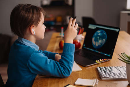 A Preteen boy uses a laptop to make online classes, globe on the screen, making notesの写真素材
