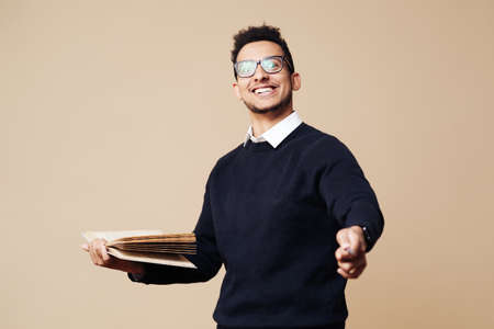 Young Professor holding a book while explaining wearing glasses on beige background. People emotions and education conceptの写真素材
