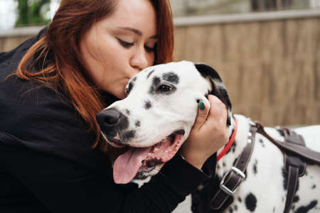 Happy woman kissing her dalmatian dog during a urban city walk. Friendship, love and care conceptの写真素材