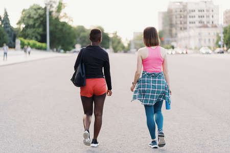 Friends back view in sportswear walking after a sport session in the city discussing . Multiethnic women having a fitness workout jogging.の写真素材