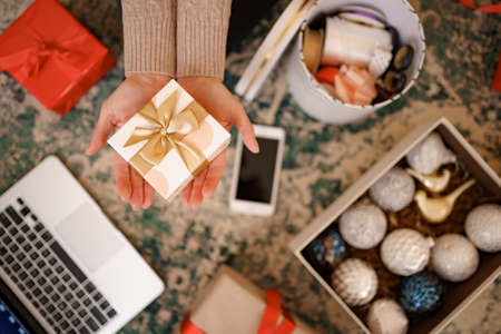 Christmas background with decorations and gift boxes. Woman hands holding wrapped white box with golden bow.の写真素材