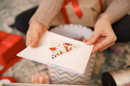 Beautiful woman hands holding a Christmas greeting card while sitting between gift boxes. Desktop coverの写真素材