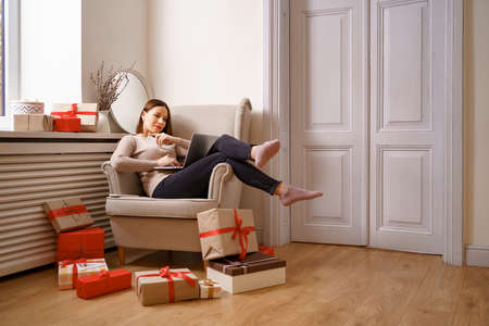 Image of pleased nice woman holding credit card with copy space using laptop while sitting on...