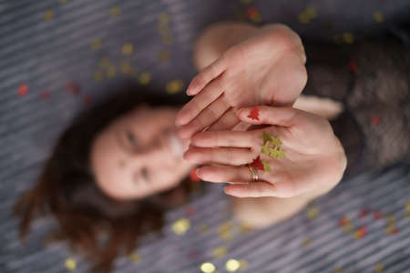 Woman lying on gray soft background decorated with golden confetti in her hands, focus on stars. Advertising, celebration conceptの写真素材