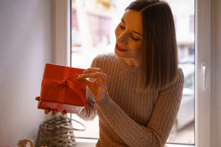 Photo of attractive smiling young woman hold a red gift box ribbon dressed in a Champaign sweater...
