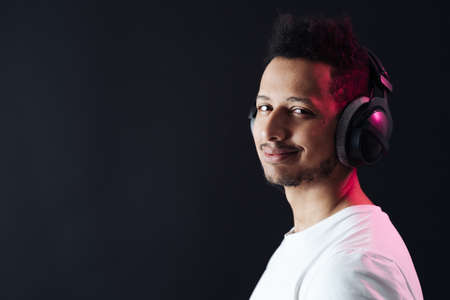 Smile Young African American man portrait wearing headphones and enjoy music over black Background...
